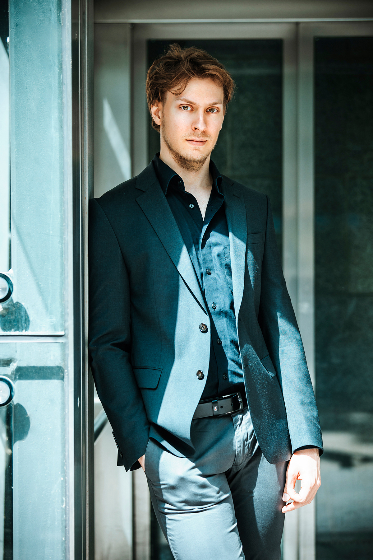 This is a picture of the extraordinarily handsome Yours Truly. I am standing in front of a door. I have short brownish hair, a mischievous smirk, and I am wearing a gray and black suit.
